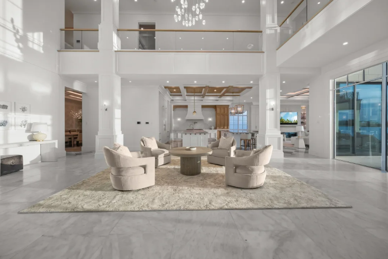 Bright modern living room with white walls, beige chairs, and large windows overlooking the water