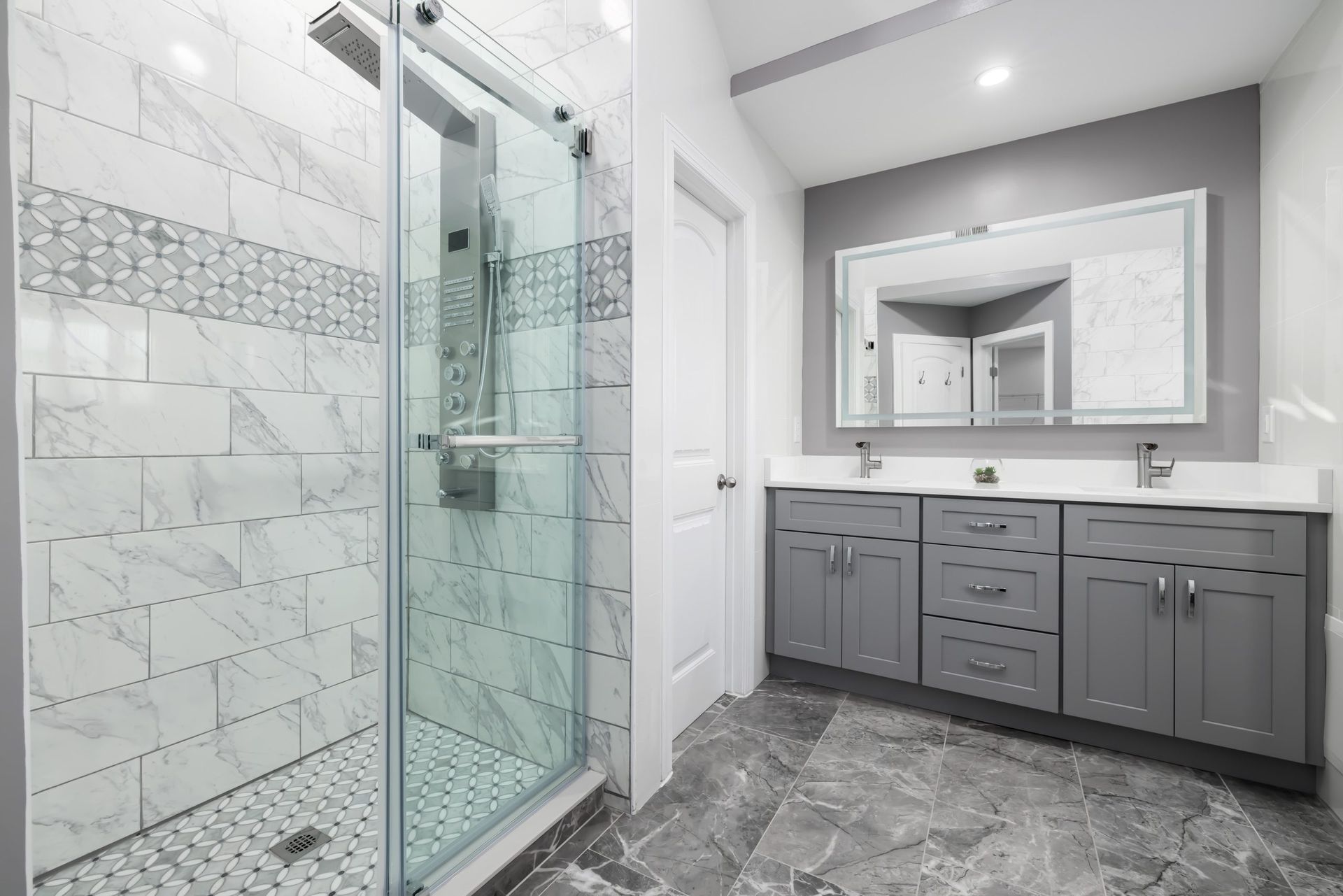 Modern bathroom with glass shower, gray vanity, large mirror, and gray tile flooring