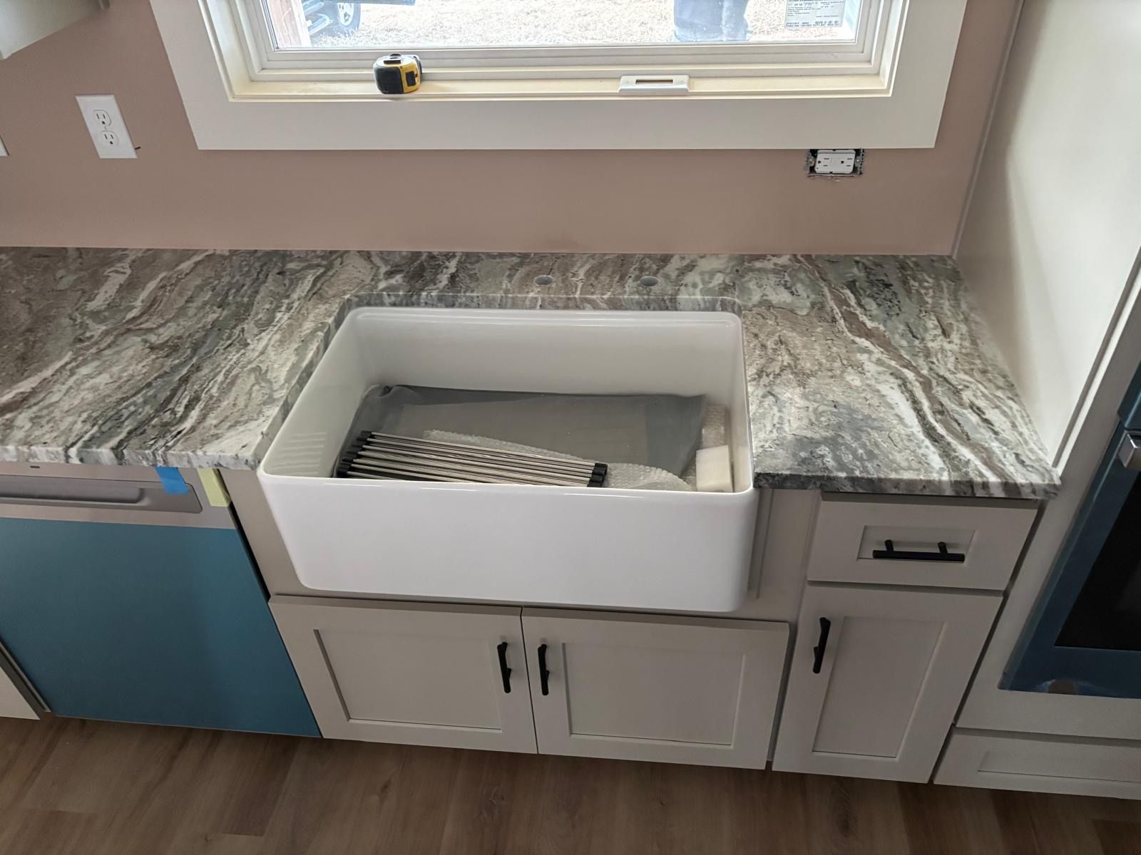 Kitchen counter with farmhouse sink, gray marble-look countertop, and blue cabinets under a window.
