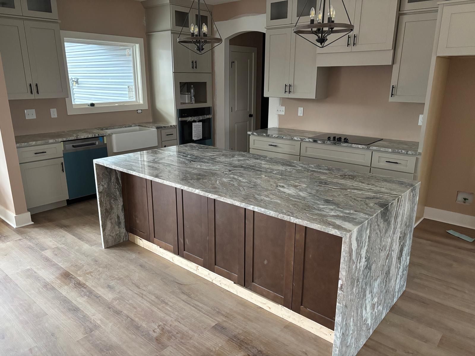 Modern kitchen with large granite island, white cabinets, and light wood flooring