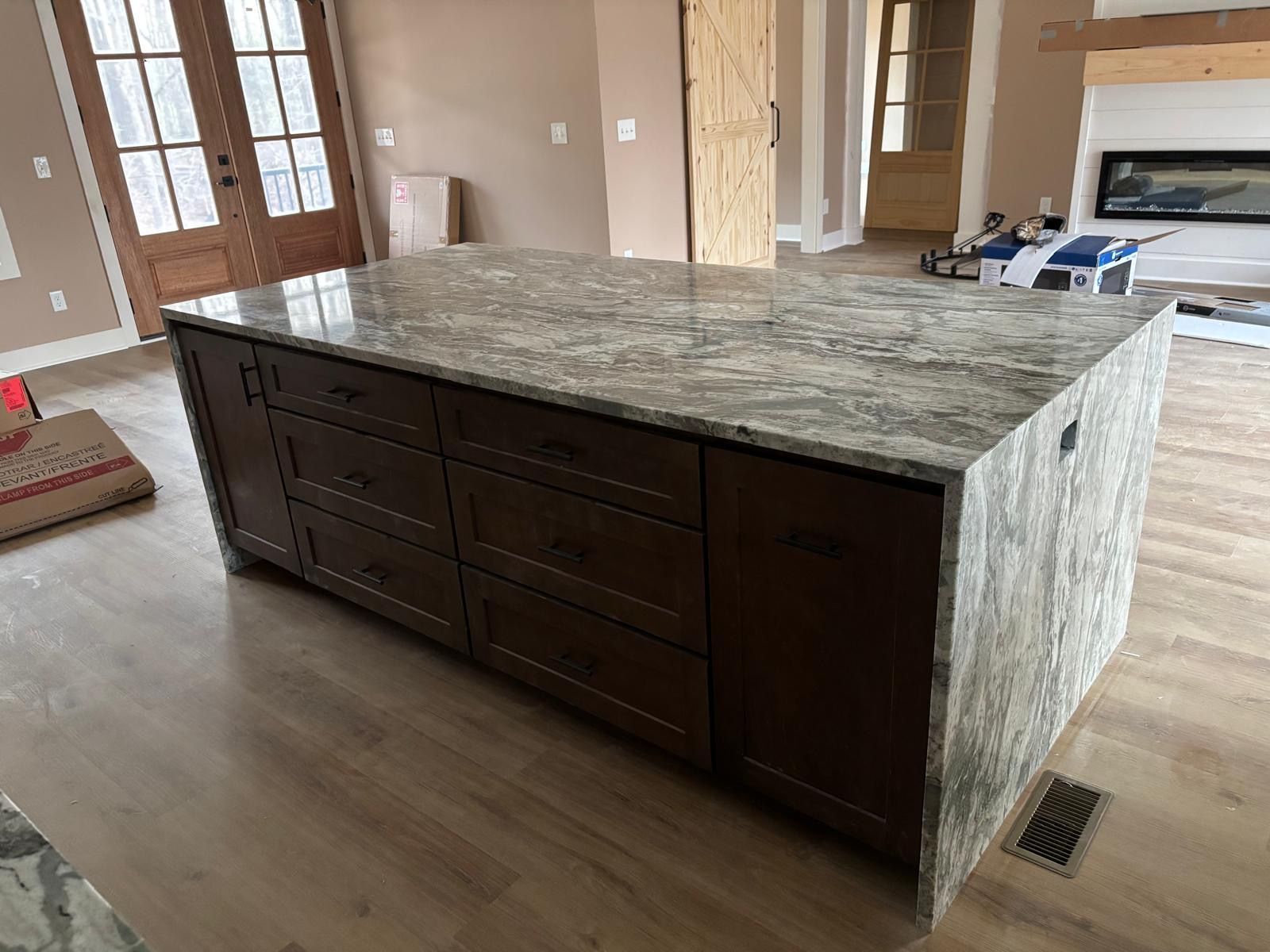 Kitchen island with dark wood cabinets and a gray stone countertop in an unfinished room