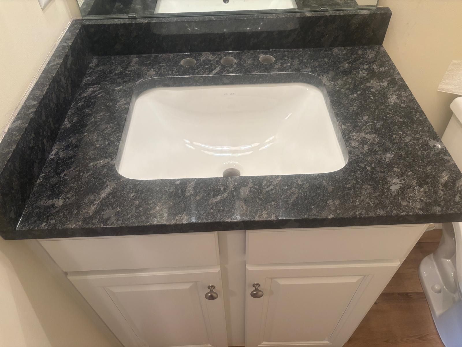Bathroom vanity with white sink and dark granite countertop, seen from above.
