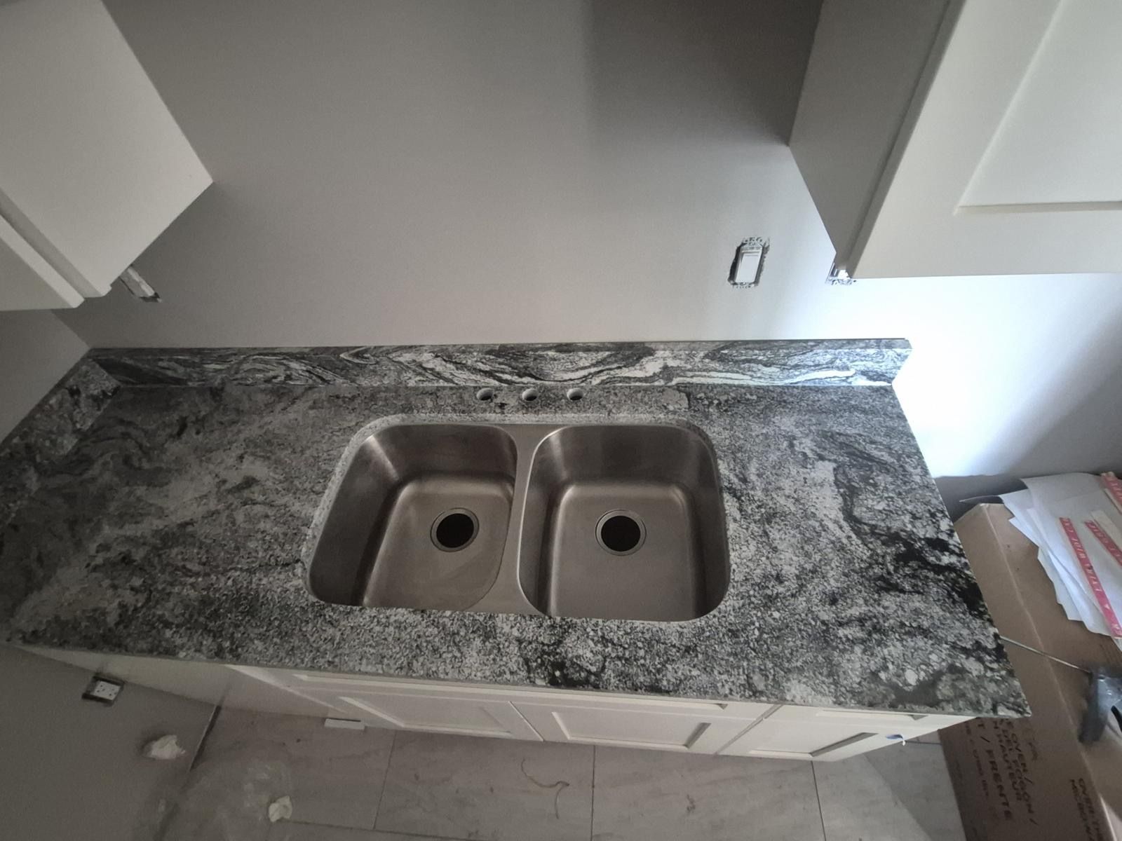 Top-down view of a kitchen countertop with a double stainless steel sink and gray granite surface