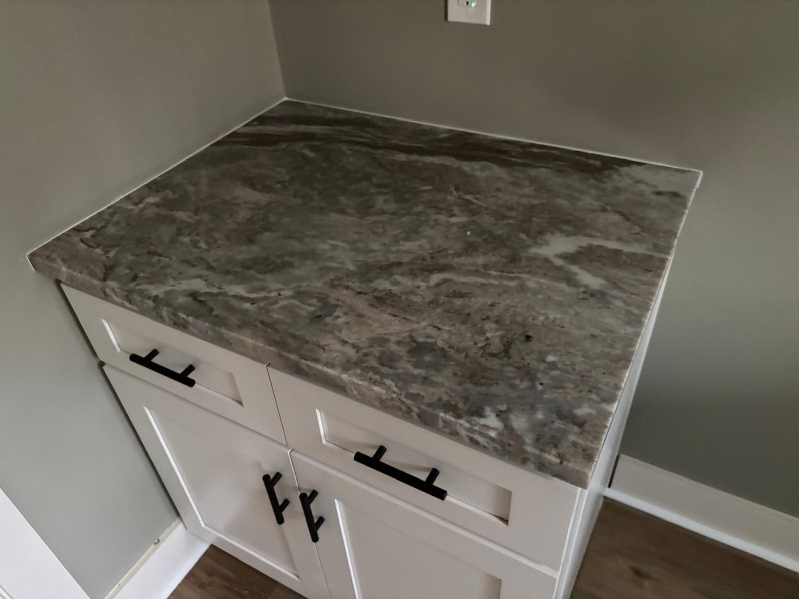 White cabinet with gray countertop in a corner, featuring black handles in a kitchen or bathroom setting