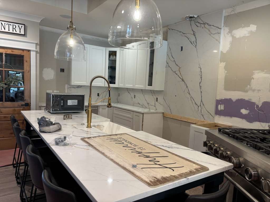 Modern kitchen with marble island, pendant lights, dark stools, and large wall tiles under renovation