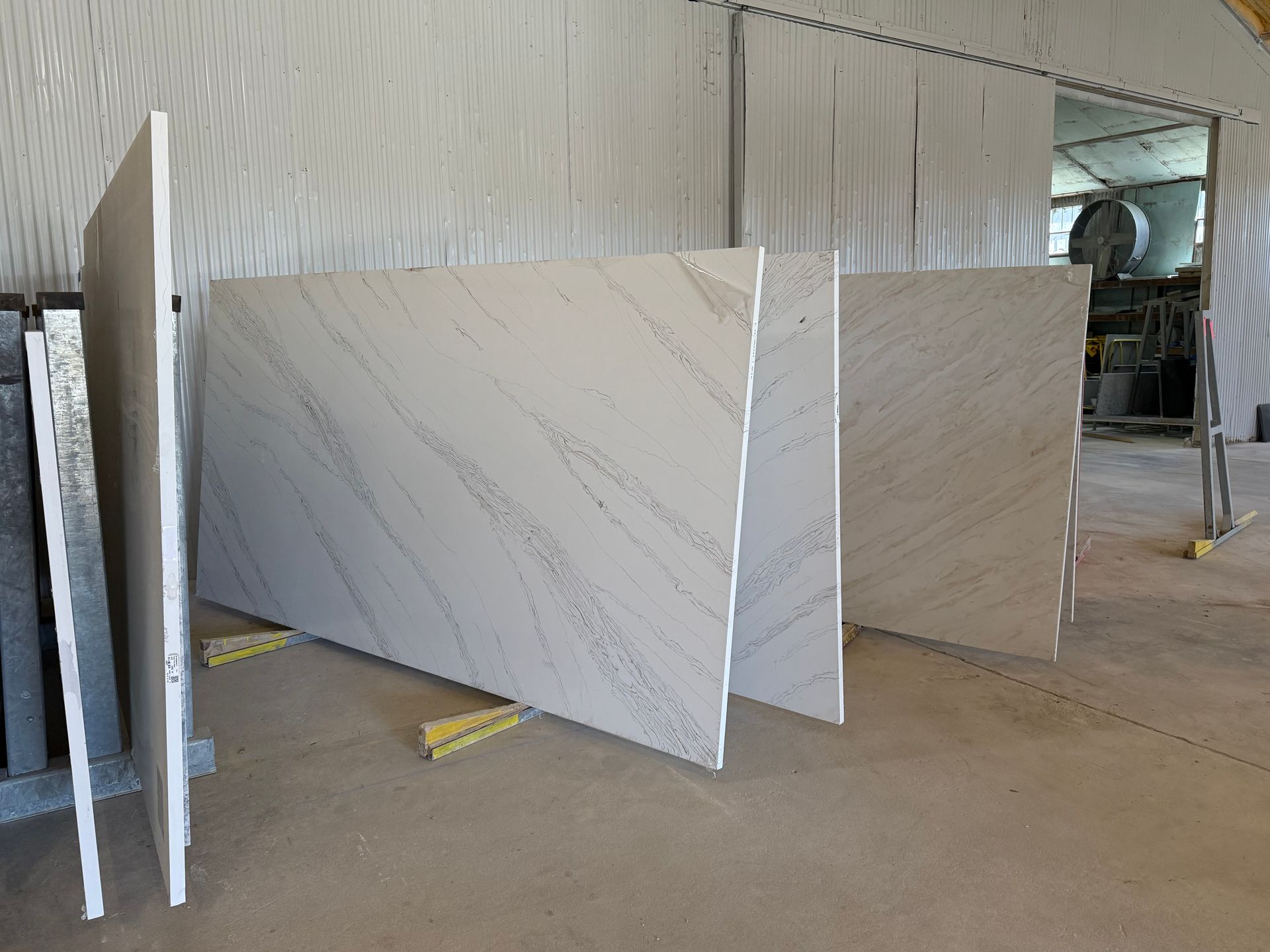Large white marble slabs standing in a workshop or warehouse, arranged in rows on the floor.