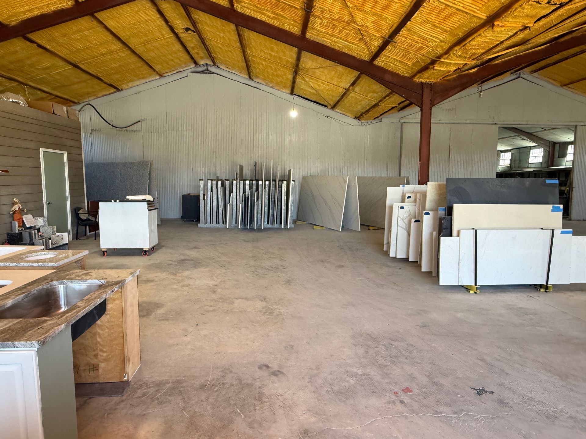 Large empty warehouse with corrugated metal walls, stacked panels, and cabinets under a yellow roof.