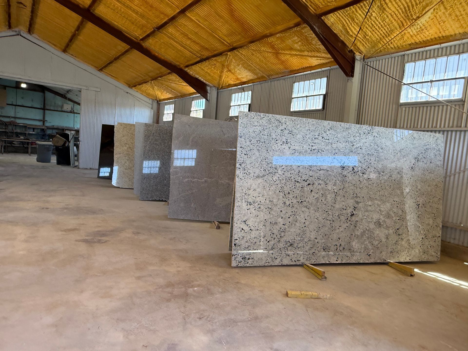 Interior of a warehouse showing large rectangular stone slabs stored under a high wooden roof