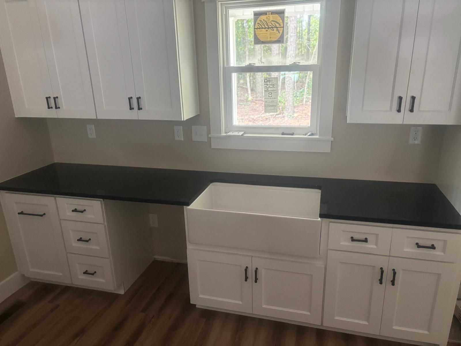 Bright white kitchen with black countertops, farmhouse sink, and window above the sink