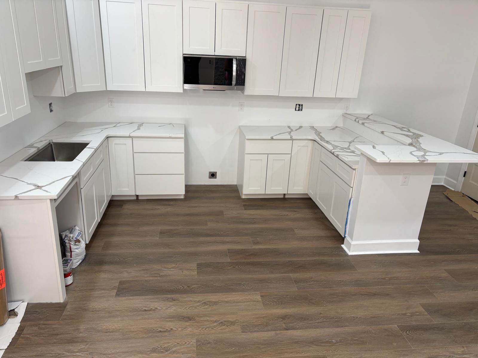 White U-shaped kitchen with cabinets, countertop, sink, and wood-look flooring.
