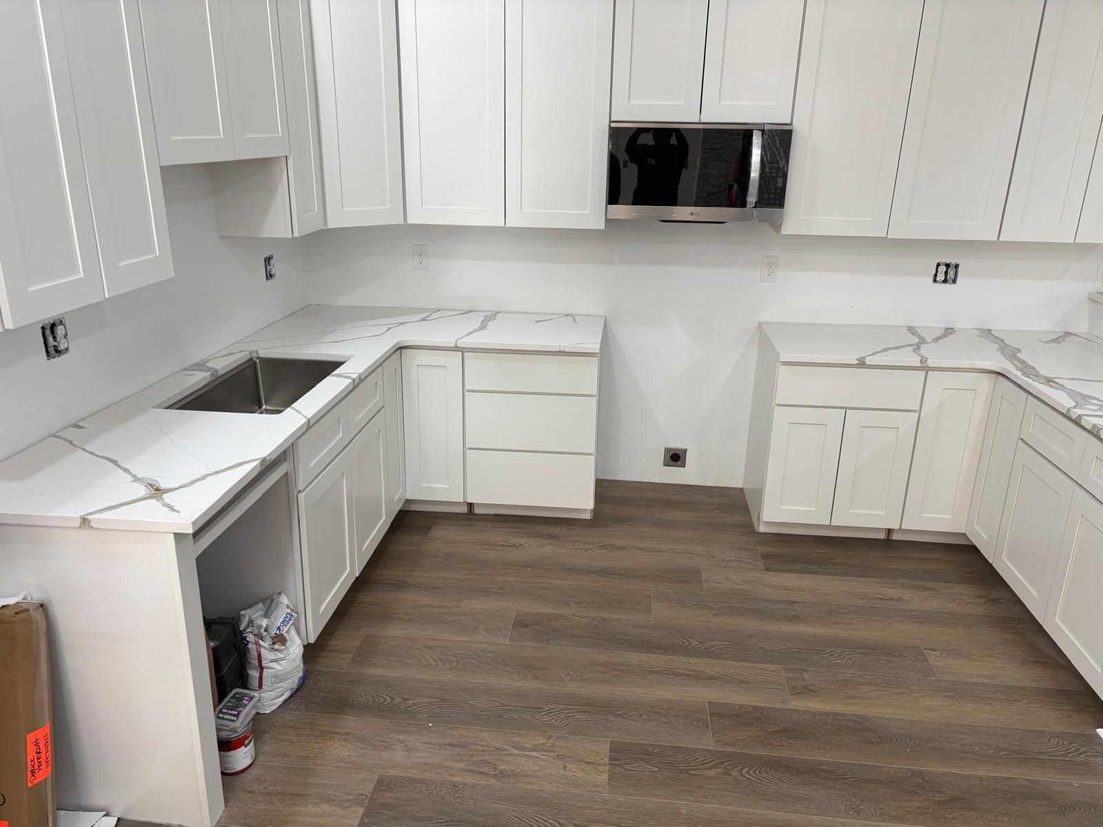 White kitchen with unfinished cabinets, wood-look flooring, and countertops along three walls.