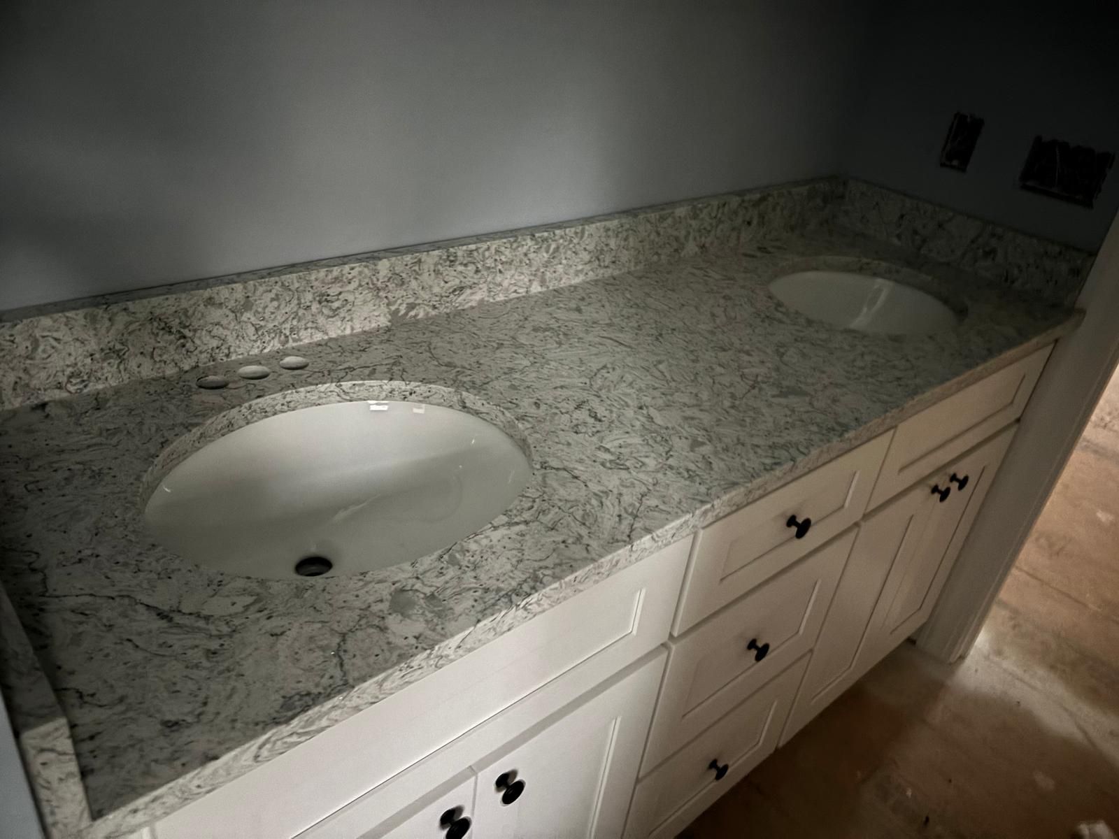Granite bathroom vanity with double sinks and white cabinets under a wall mirror