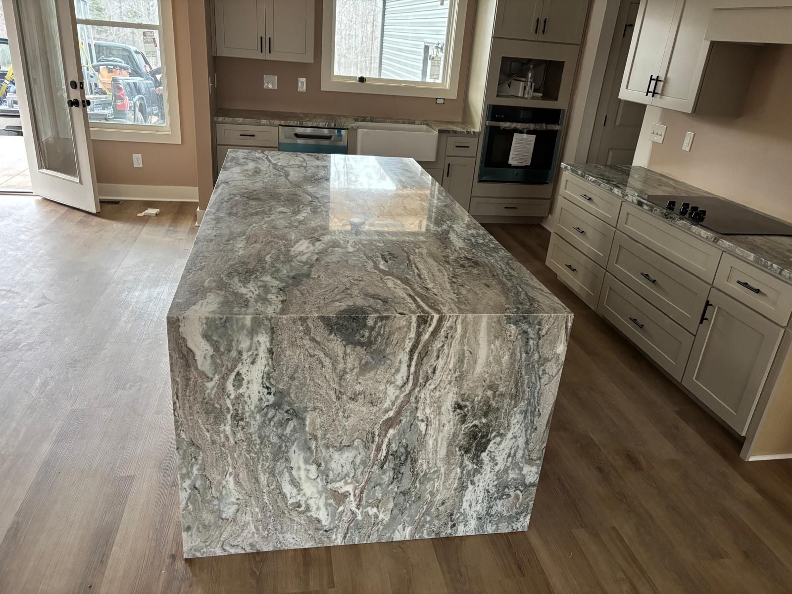 Kitchen with large gray marble island and light wood floors, viewed from the center of the room.