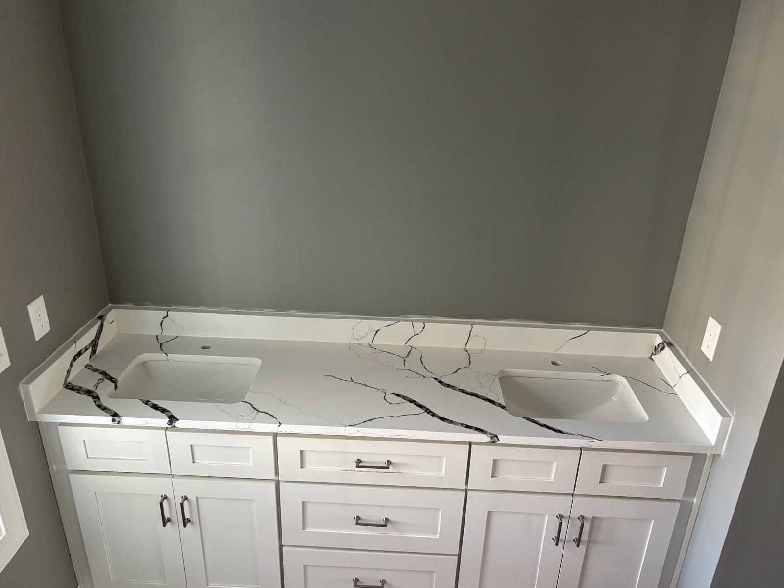 Double-sink bathroom vanity with white cabinets and marble-look countertop against a gray wall
