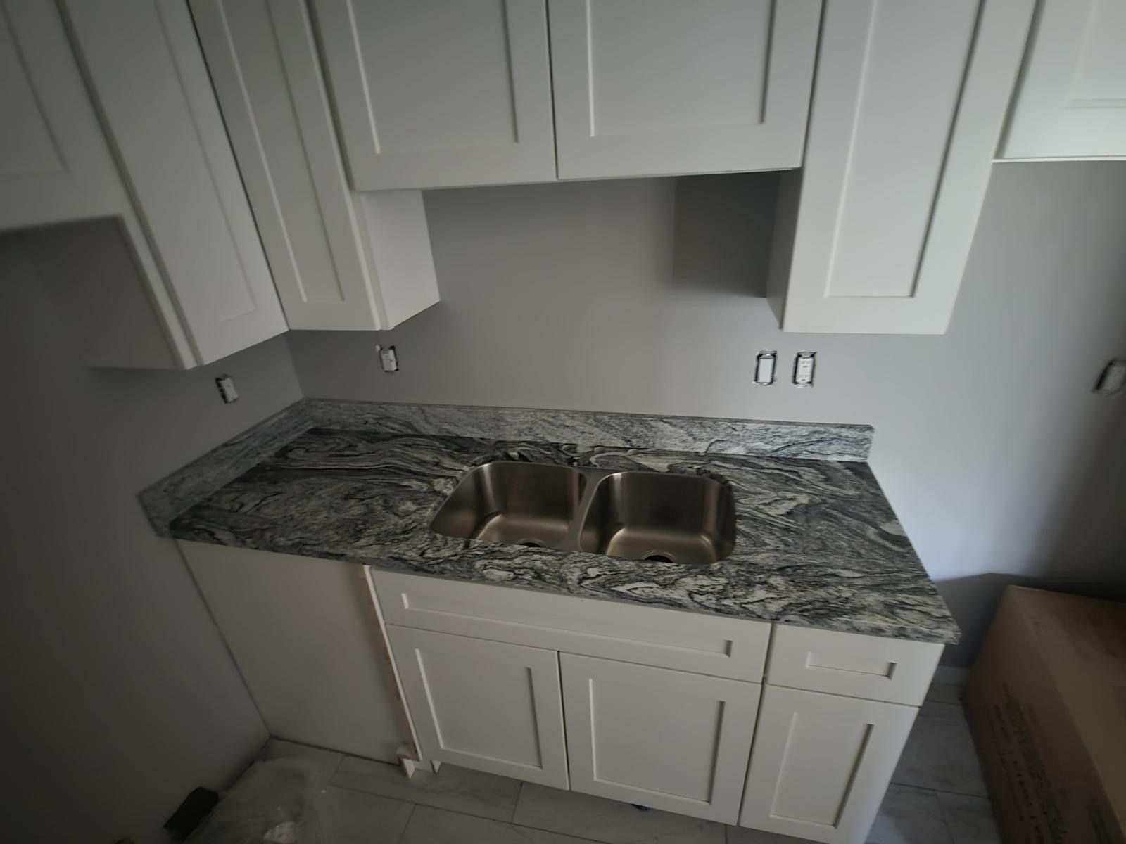 Small kitchen with gray granite countertop, stainless double sink, and white cabinets.
