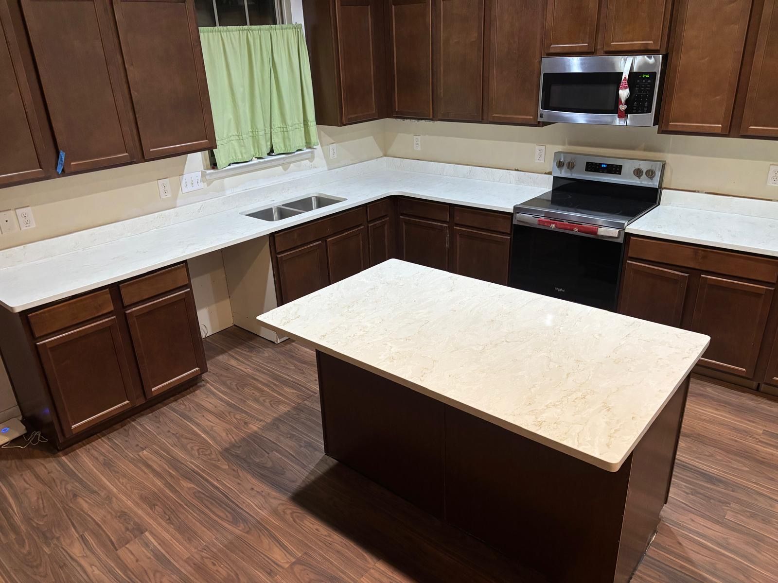 Empty kitchen with dark wood cabinets, white countertops, and a central island under warm lighting