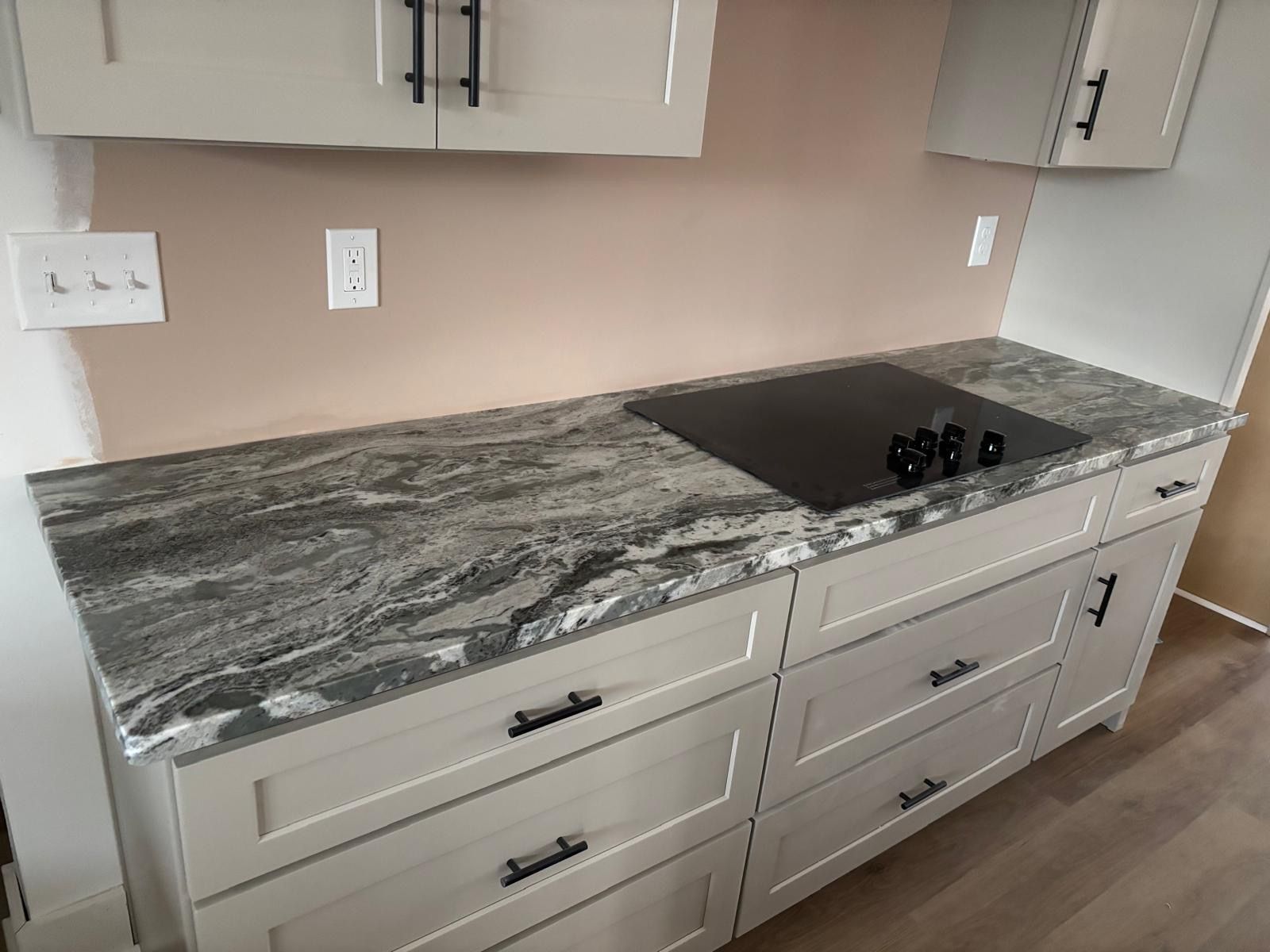 Kitchen countertop with gray marble slab, black cooktop, and light gray drawers below.