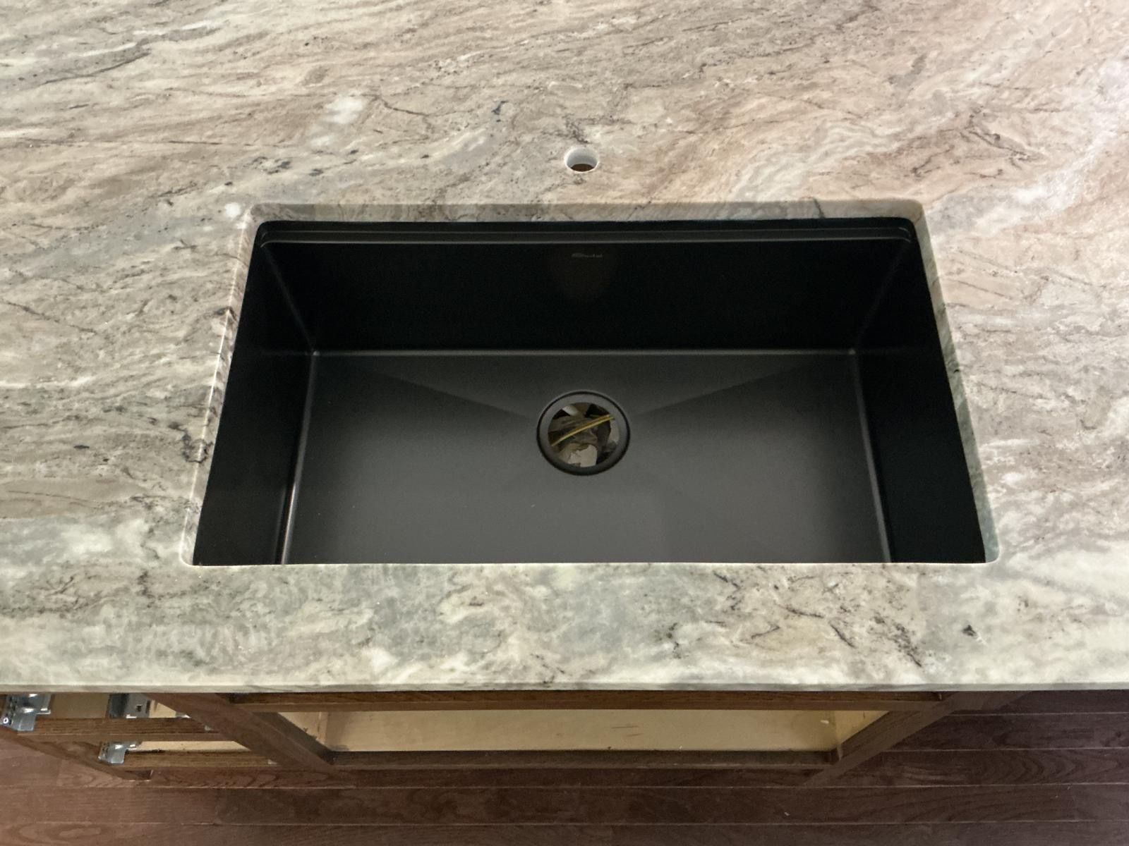 Black rectangular sink set in a light stone countertop, with a centered drain.