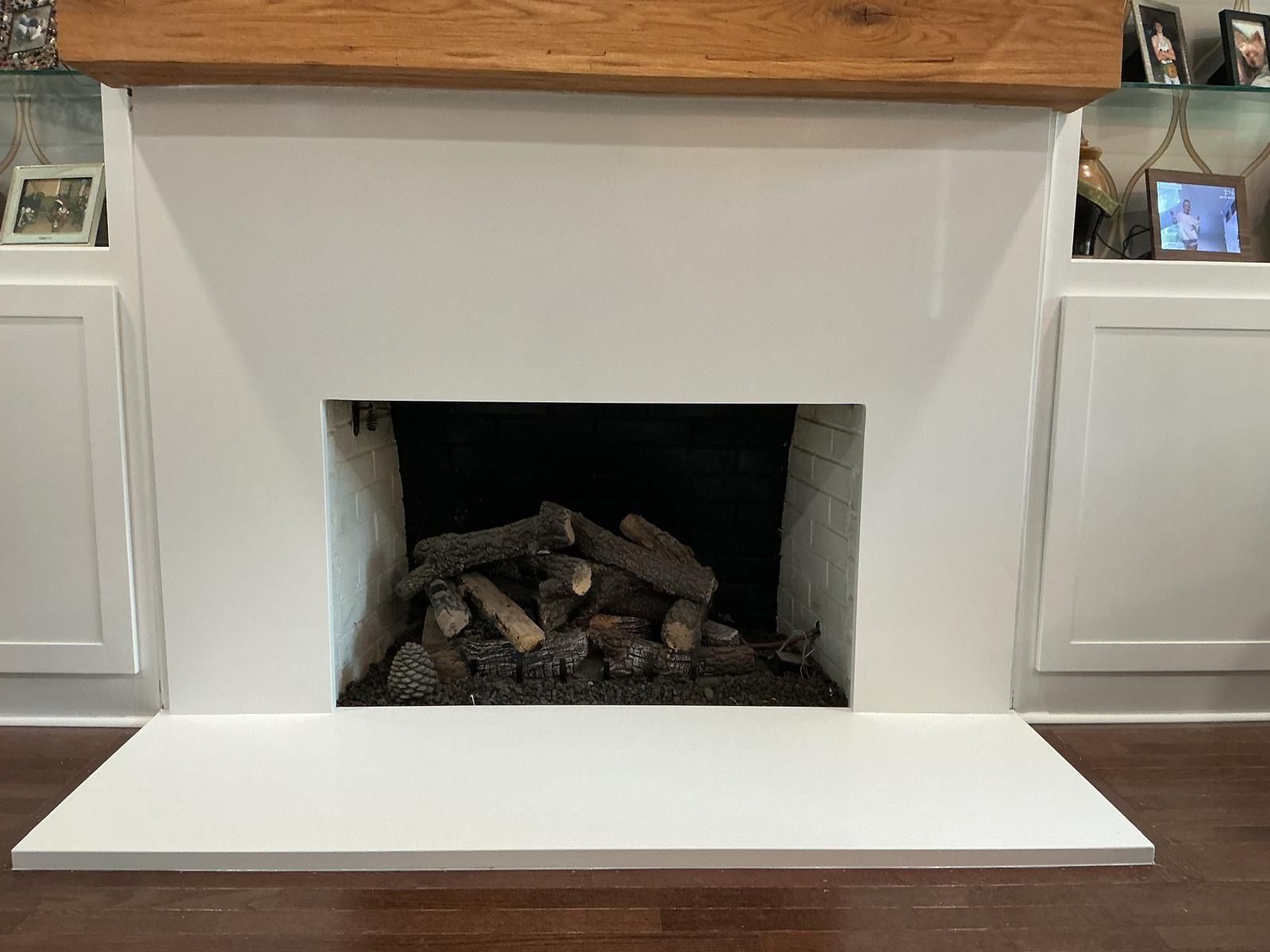 White fireplace with stacked logs and a wooden mantel in a bright living room