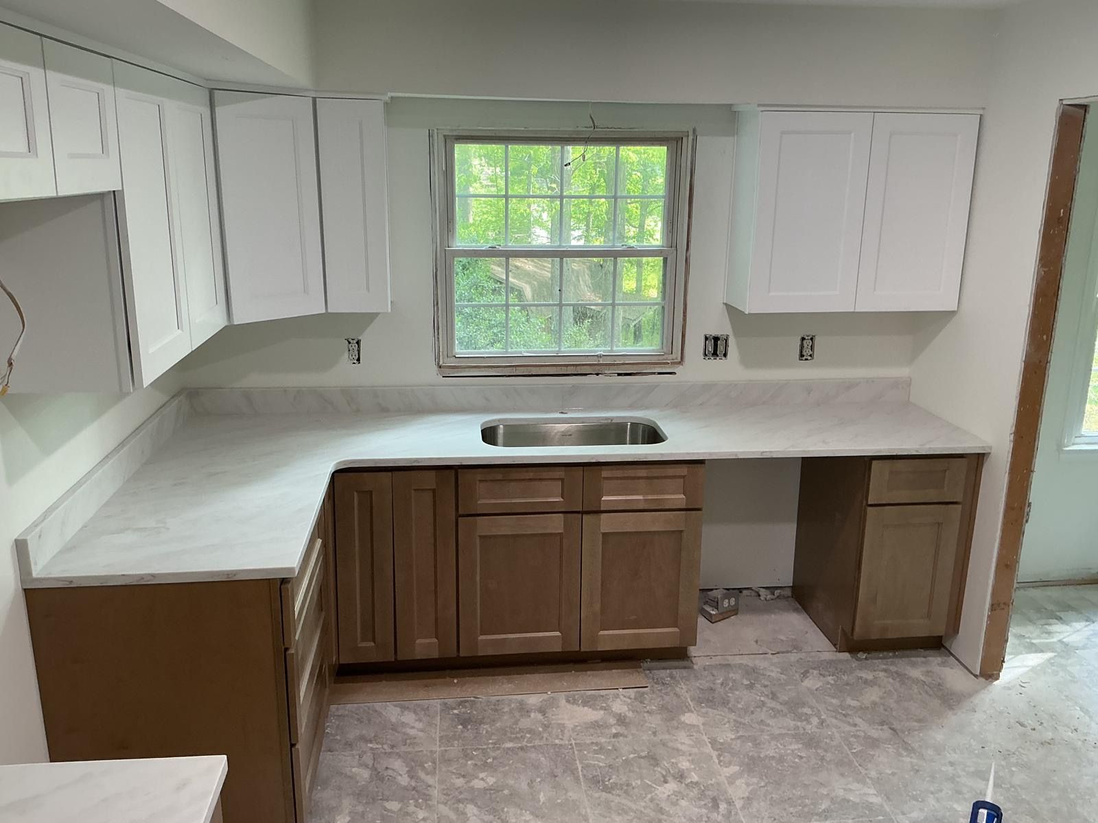 Empty kitchen with white cabinets, wood lower cabinets, and a window above a sink.