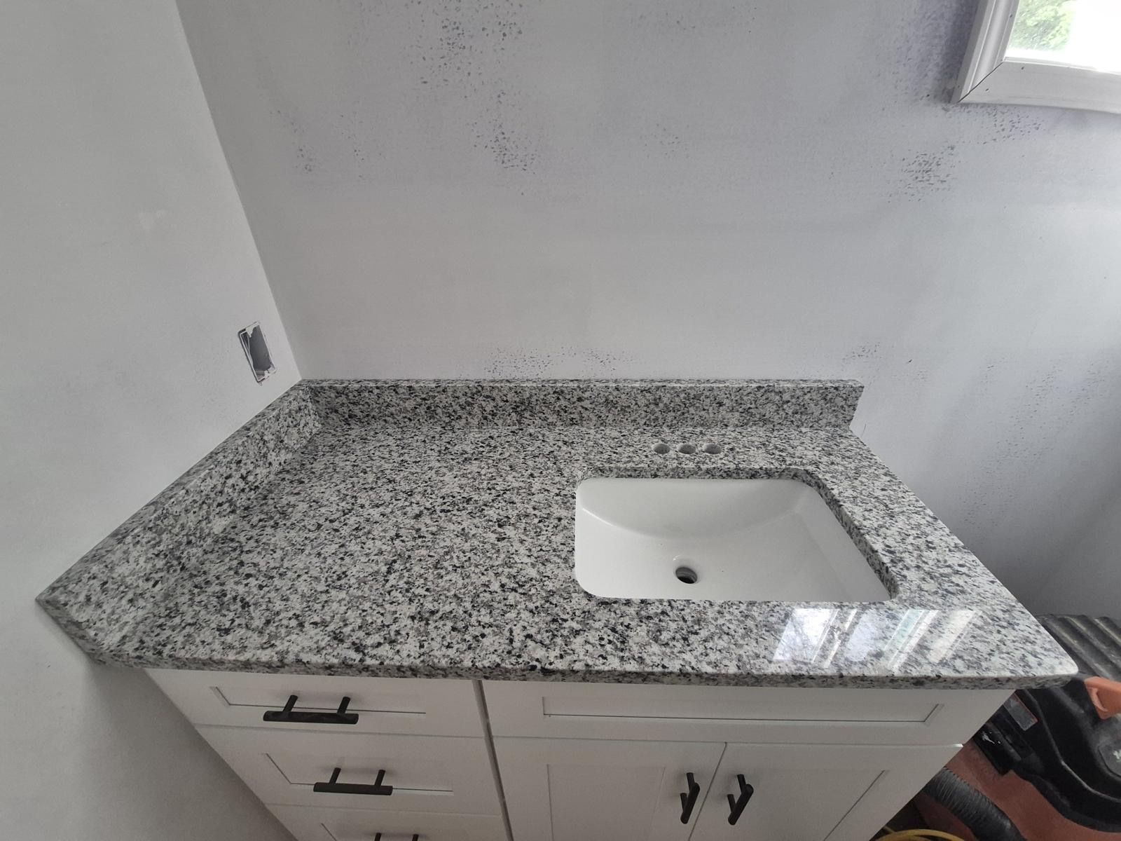 Granite bathroom vanity with white sink and cabinet drawers against a white wall