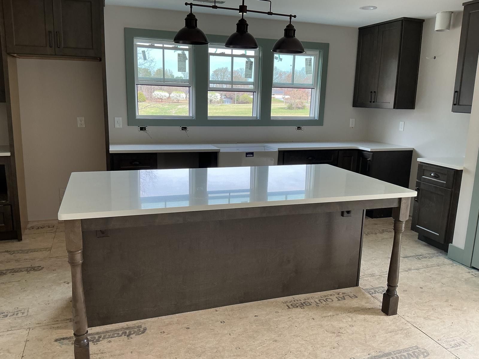 Modern kitchen with white island, dark cabinets, pendant lights, and large windows
