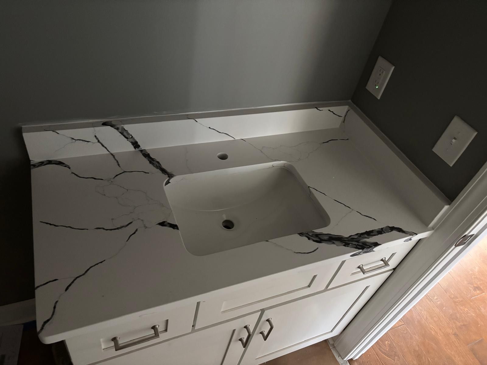 White bathroom vanity with marble-look countertop, sink, and dark gray walls next to a doorway.