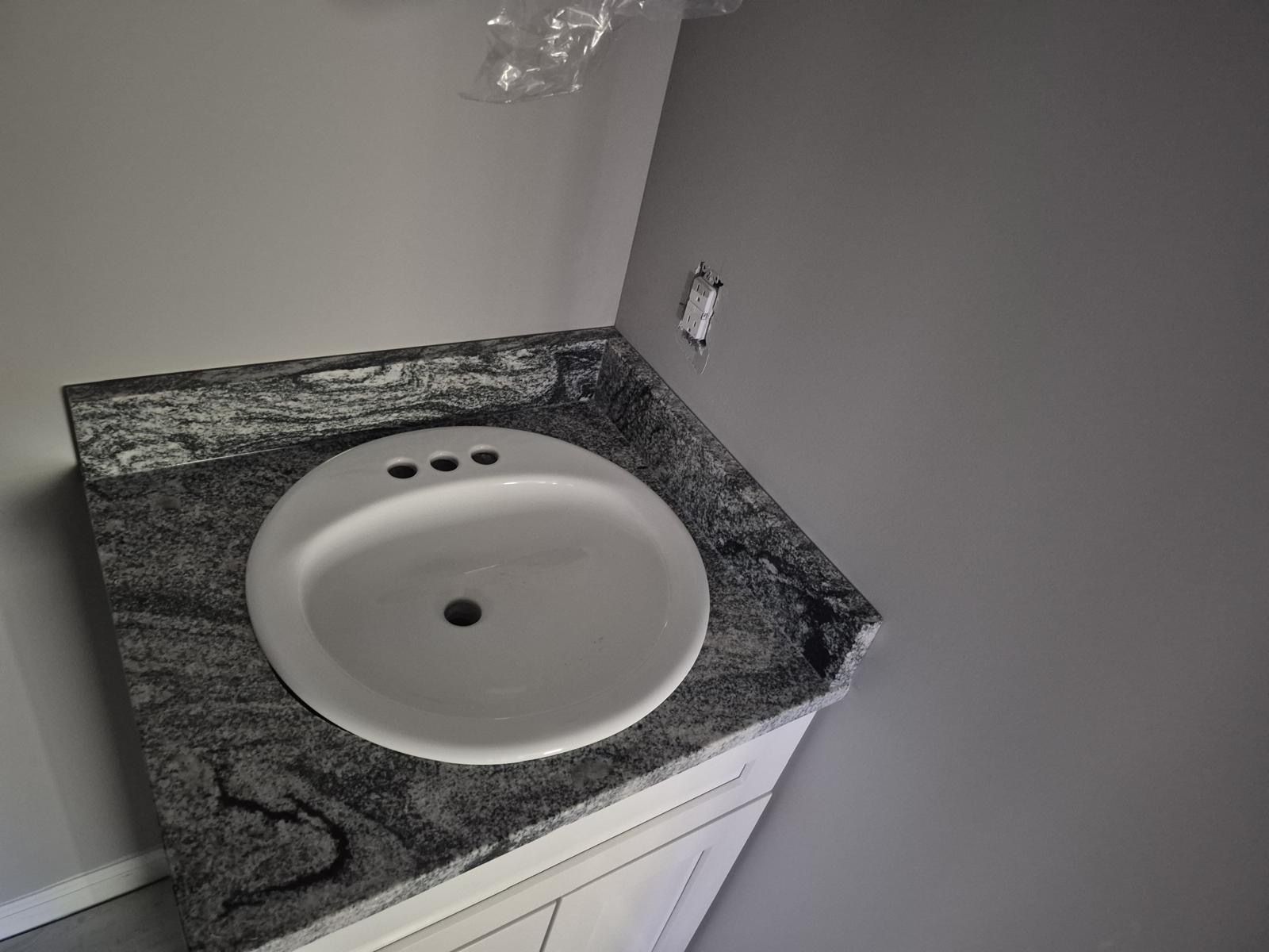 Bathroom vanity with white sink and dark granite countertop against a gray wall