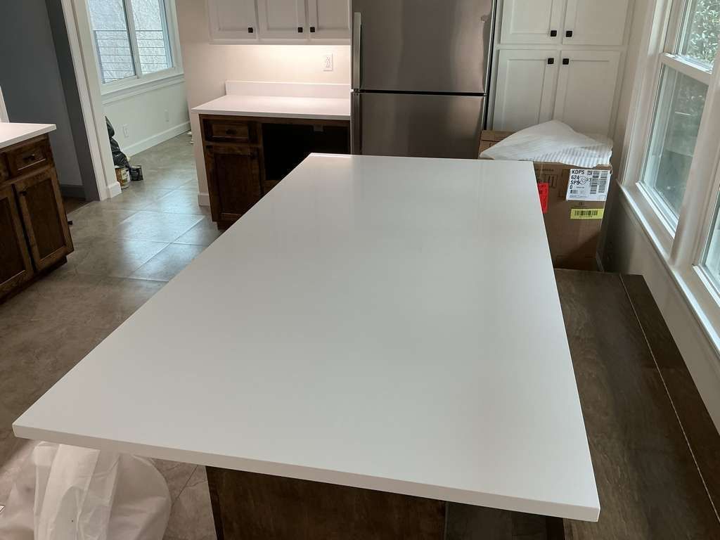 Bright white kitchen island countertop in a modern kitchen with wood floors and stainless steel appliances.