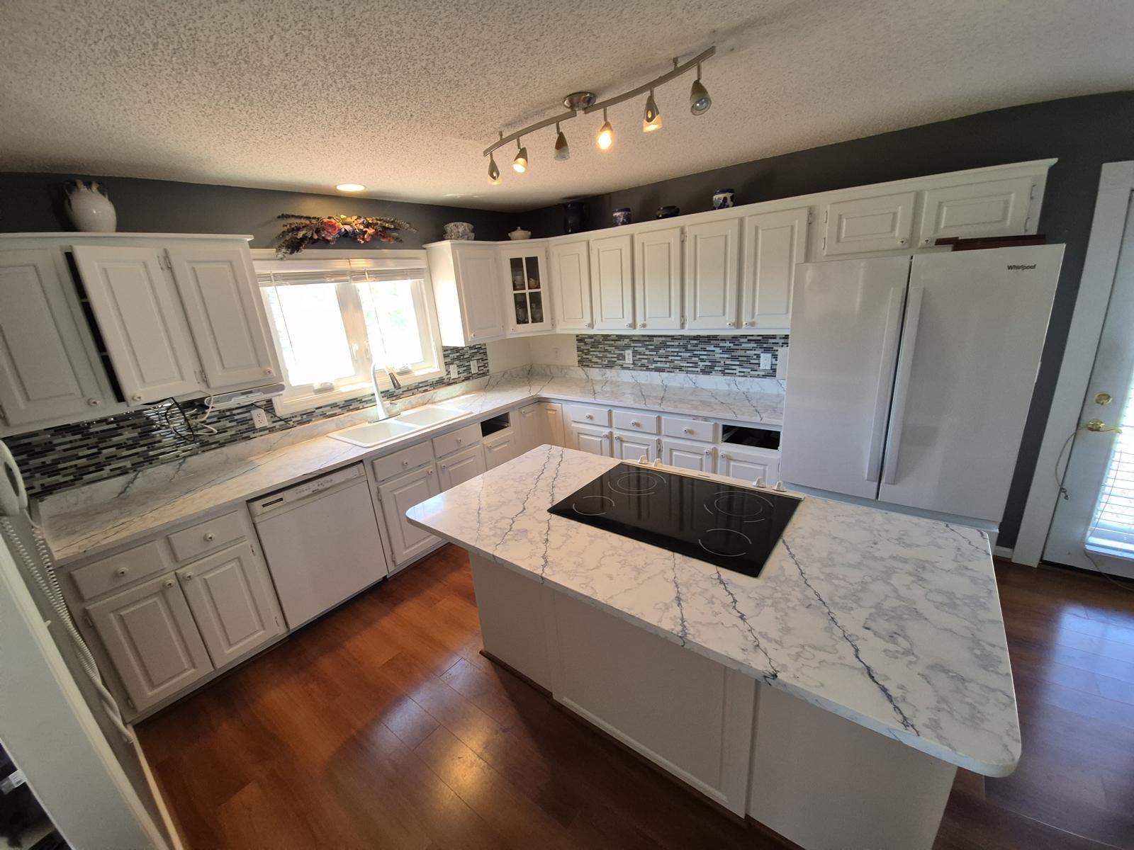 Bright modern kitchen with white cabinets, marble island, dark backsplash, and wood floors