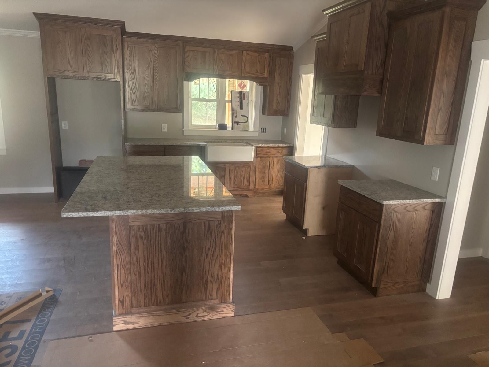 Empty kitchen with dark wood cabinets, granite island, and hardwood floors.