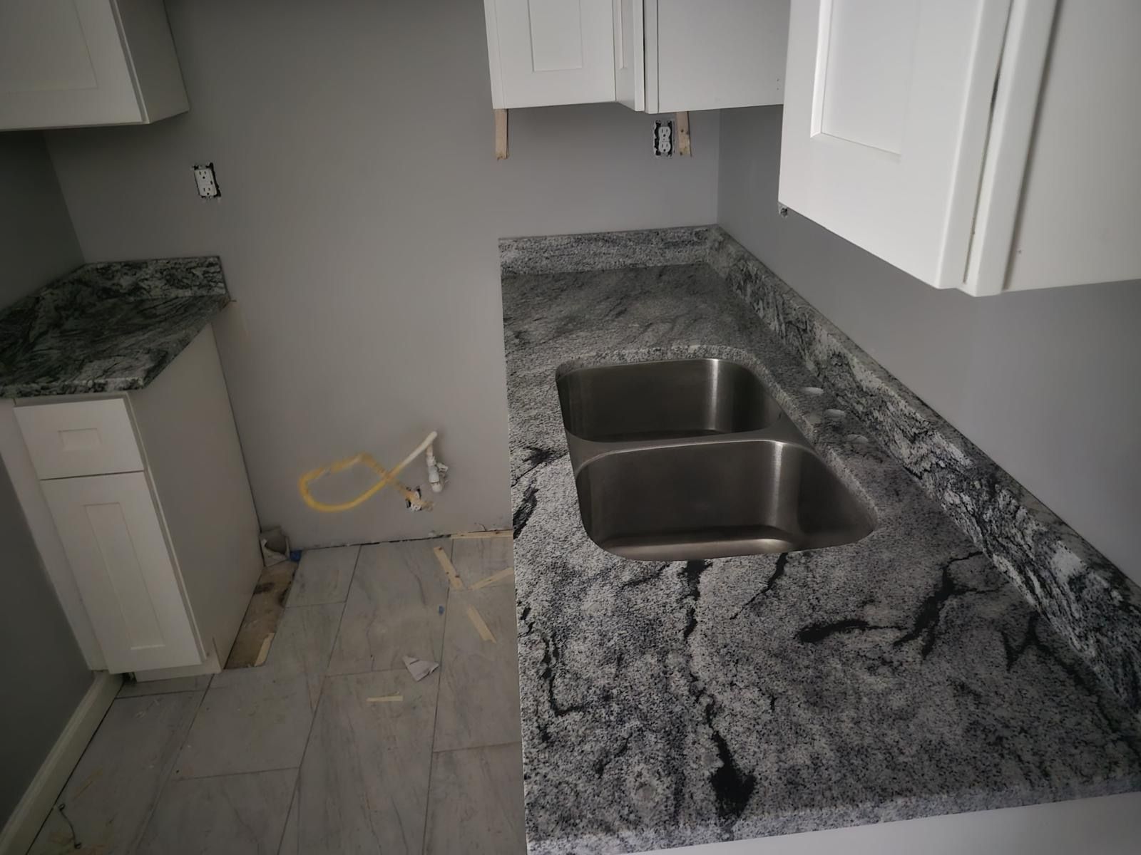 Empty kitchen with gray granite countertops, white cabinets, and a stainless steel sink.