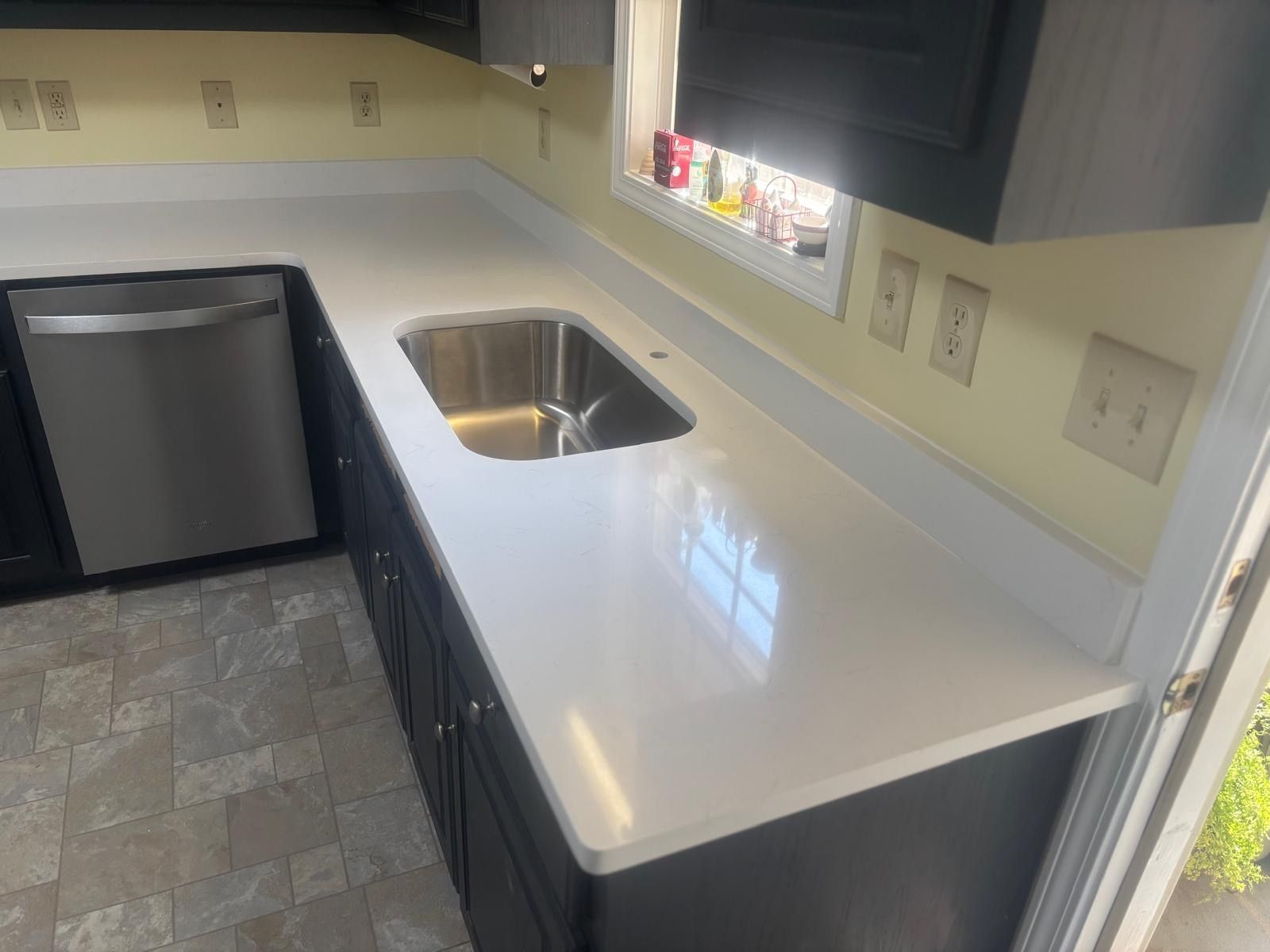 Small kitchen counter with stainless sink, white countertop, black cabinets, and tiled floor.