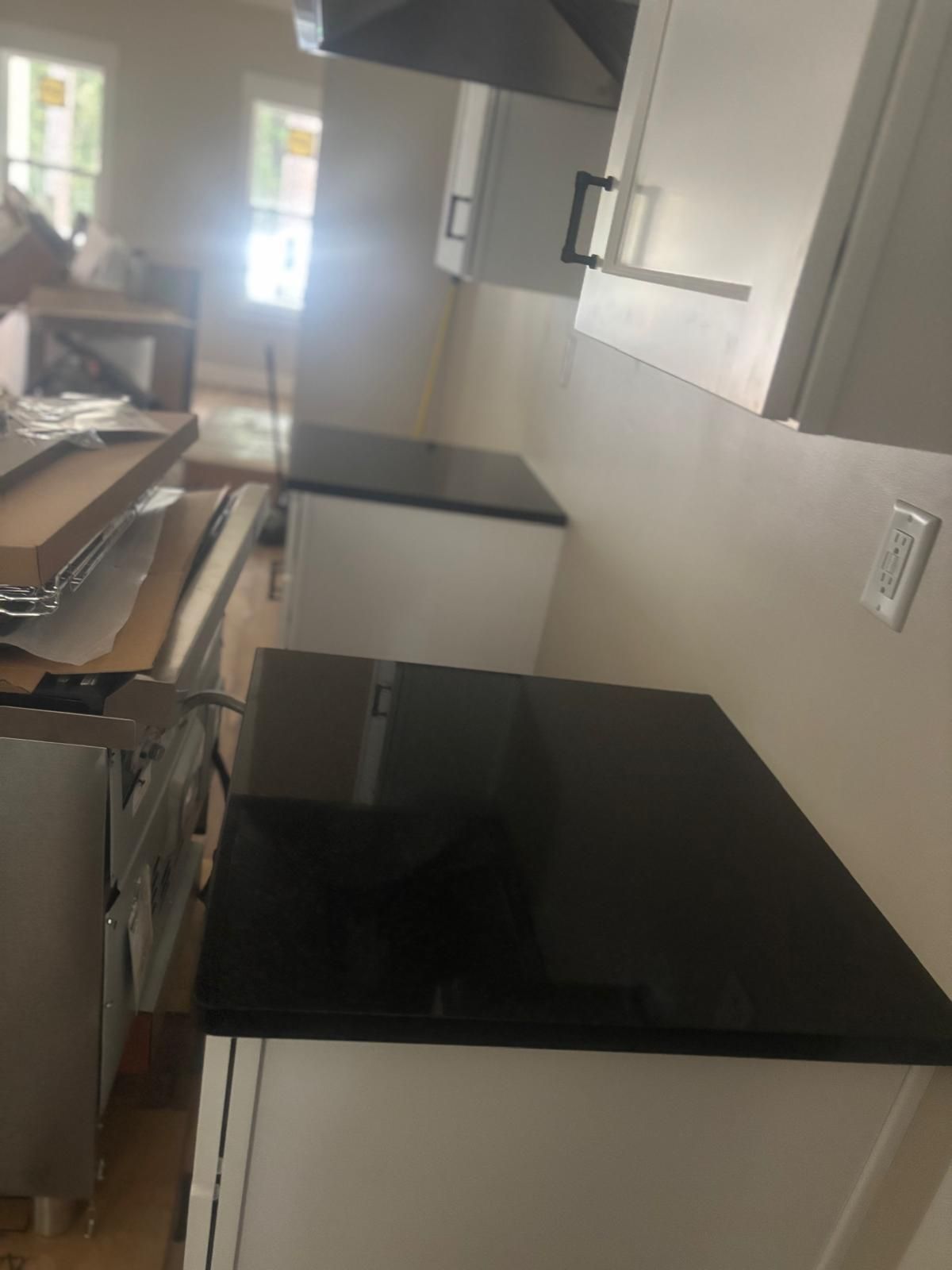 Narrow kitchen with black countertops and white cabinets, viewed down a bright hallway.