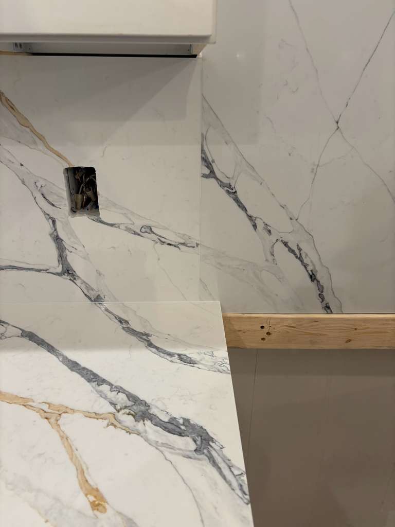Marble-pattern tile wall with a small wall opening, wood trim, and part of a cabinet above