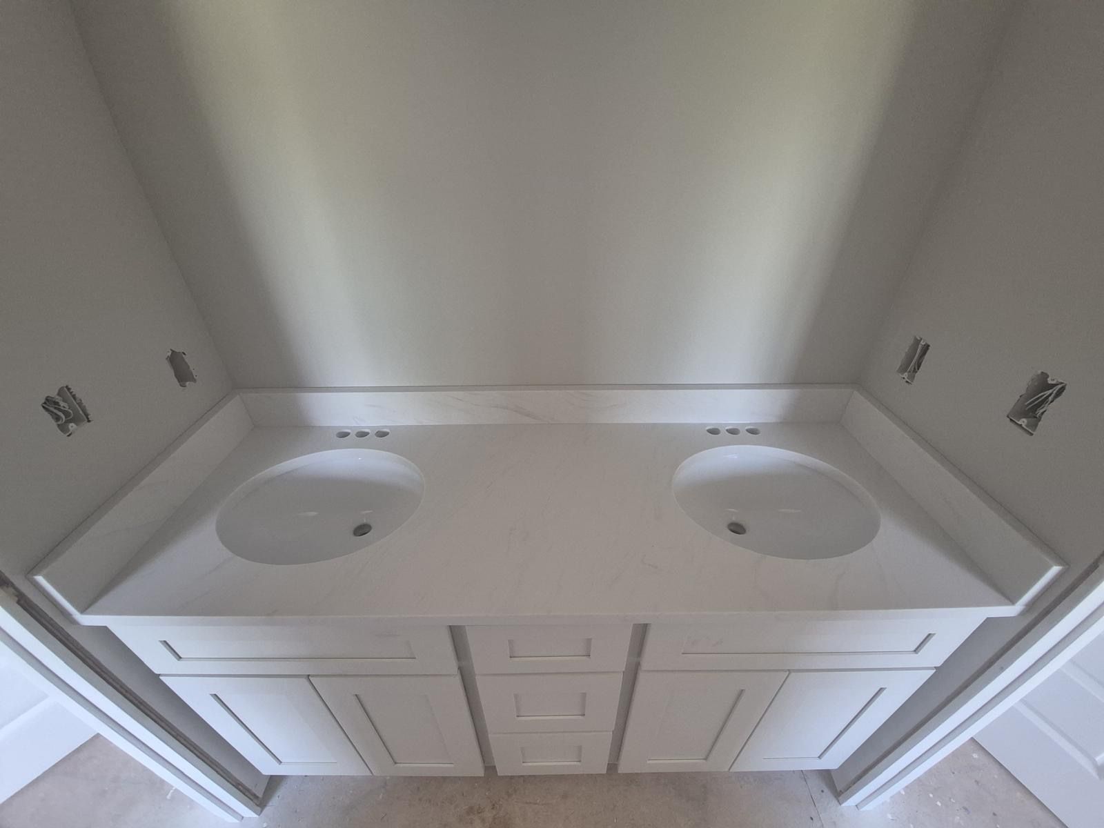 Double vanity bathroom sink with two basins, white cabinets, and a large countertop in a narrow alcove