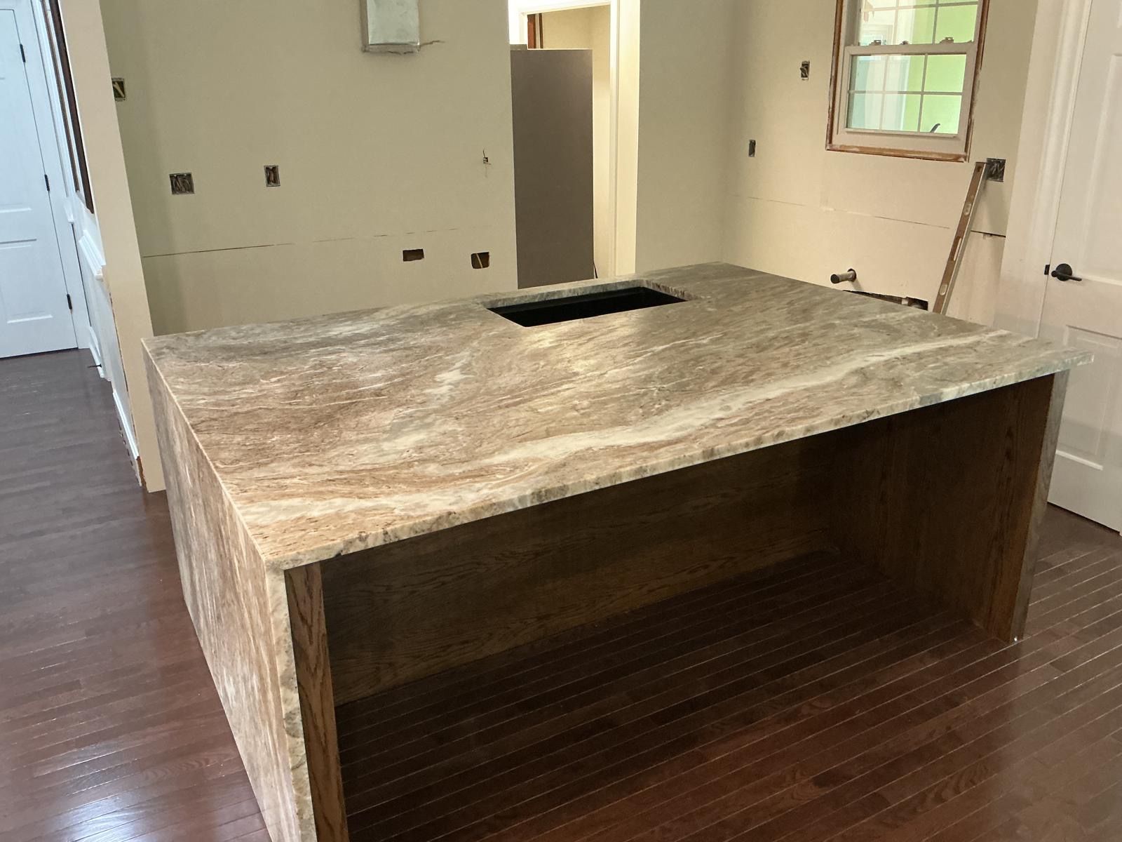 Large wooden kitchen island with a stone countertop and central cutout in an empty room