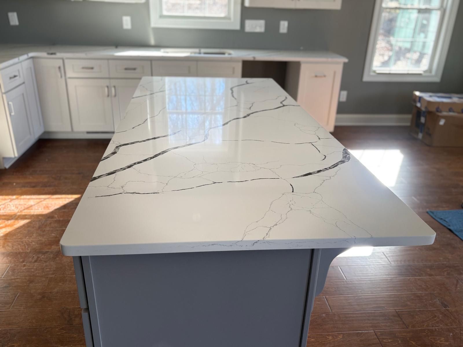 Modern kitchen with a long white island countertop and gray cabinets.