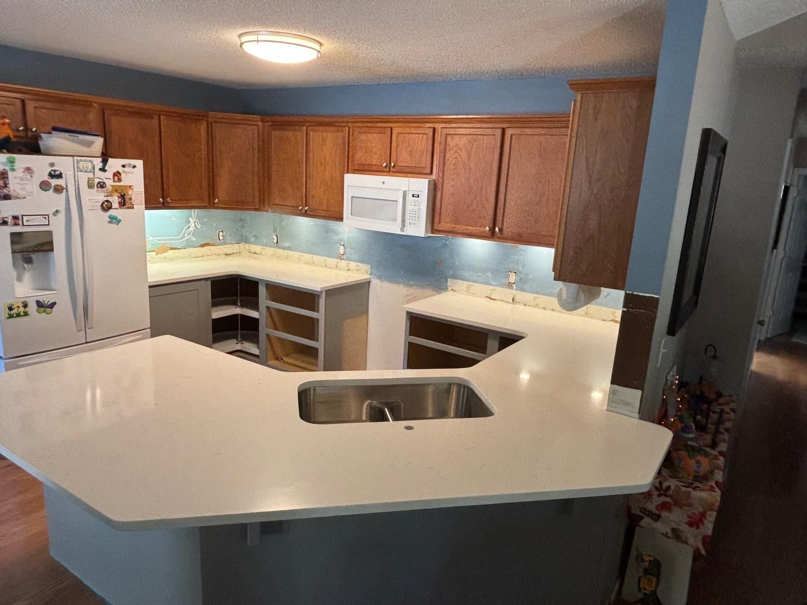 Modern kitchen with white island countertop, wood cabinets, white appliances, and blue accent lighting