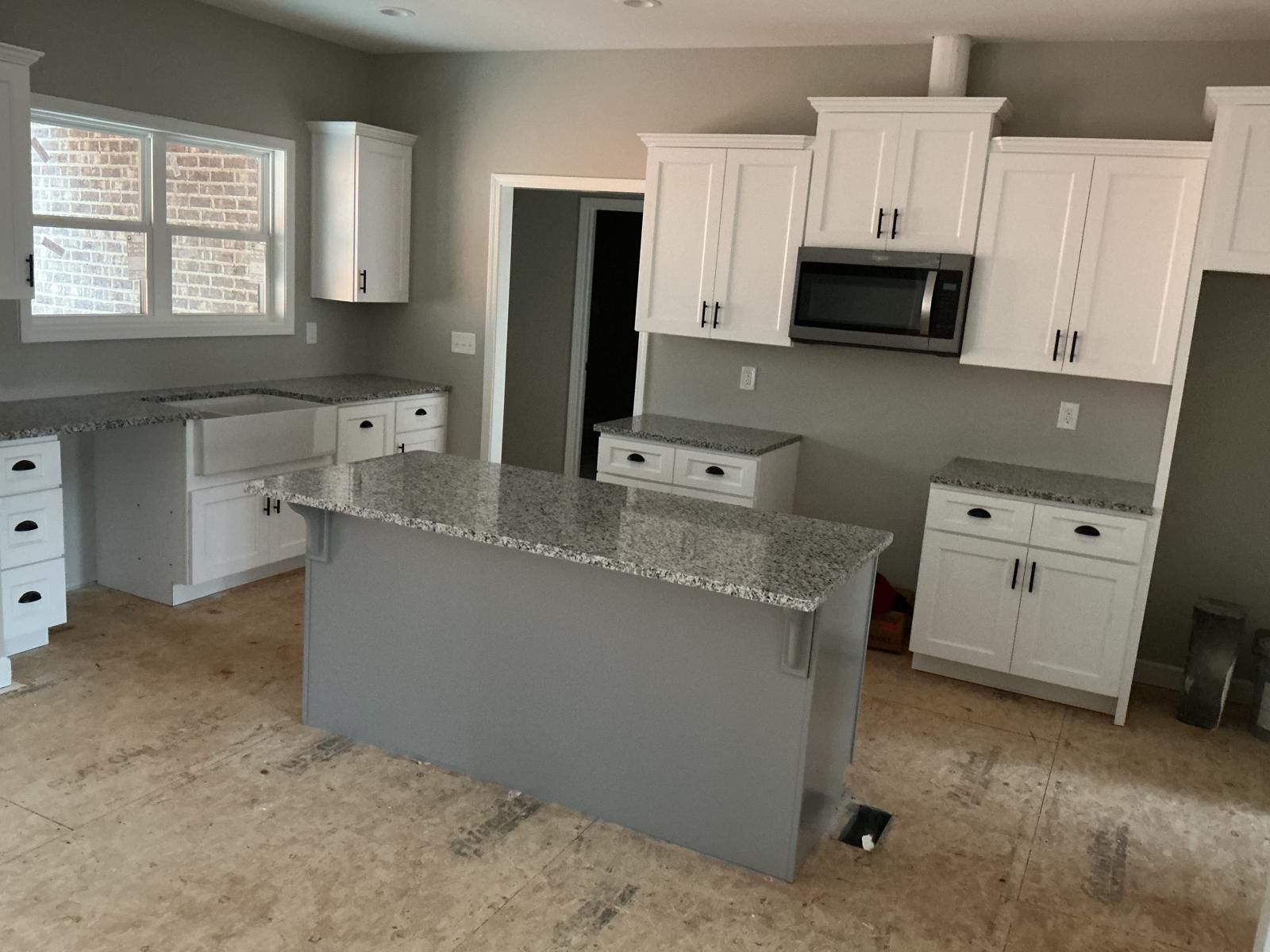 Empty kitchen with white cabinets, gray island, and granite countertops, viewed from the dining area.