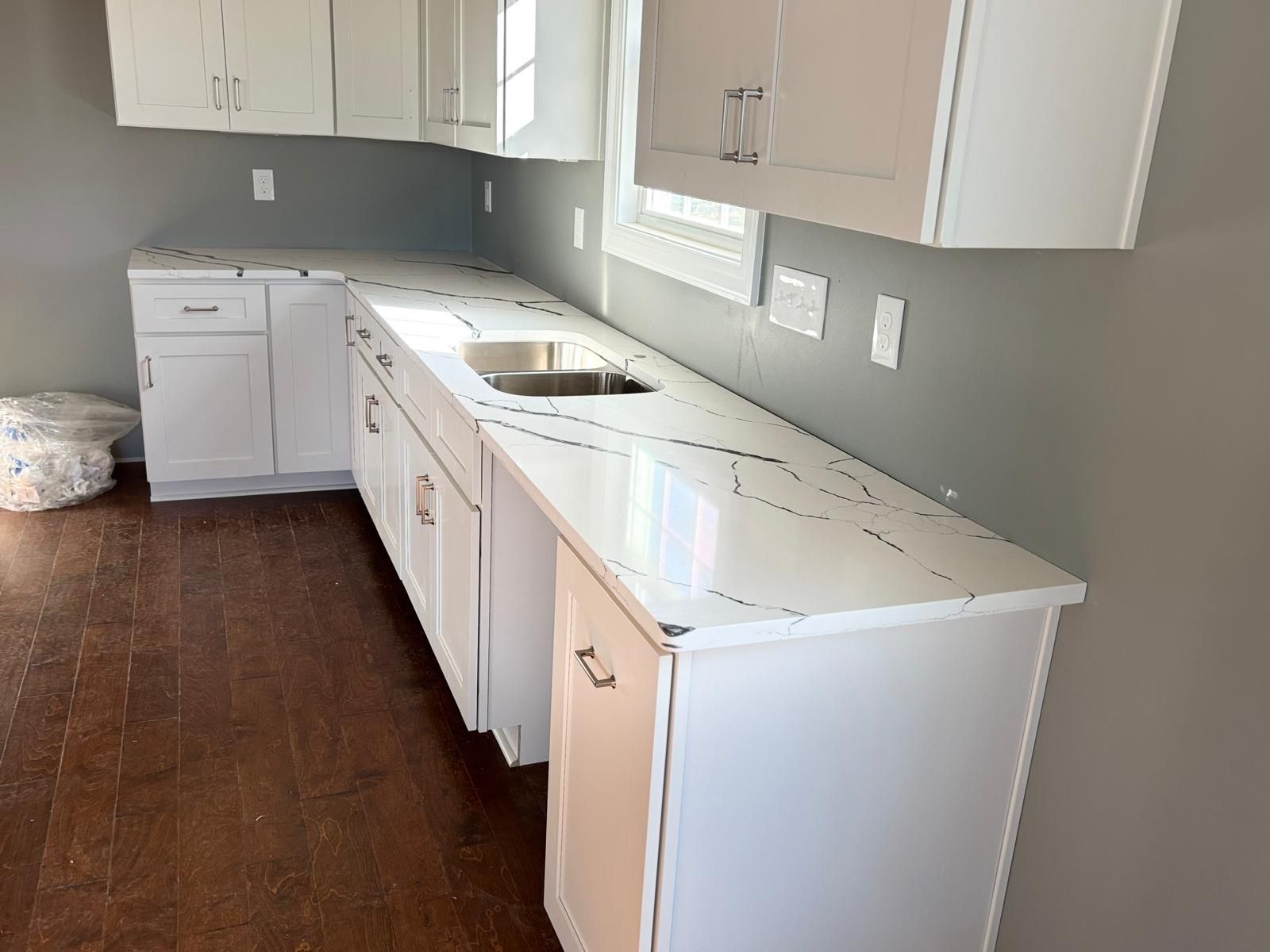 Unfinished kitchen with white cabinets and countertops, gray walls, and dark wood flooring.
