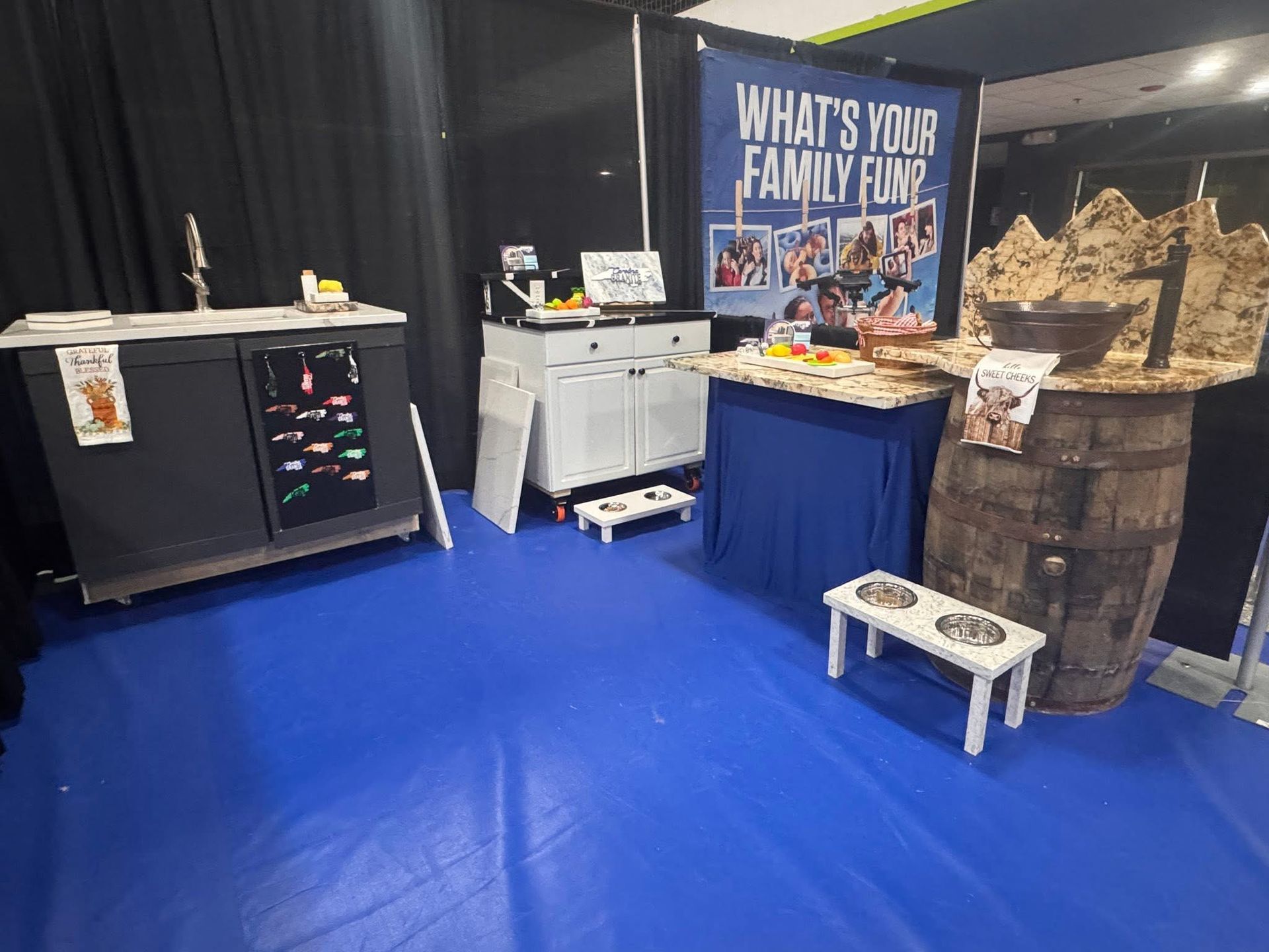 Expo booth with blue carpet, black curtains, display tables, and a sign reading “What’s Your Family Fun?”
