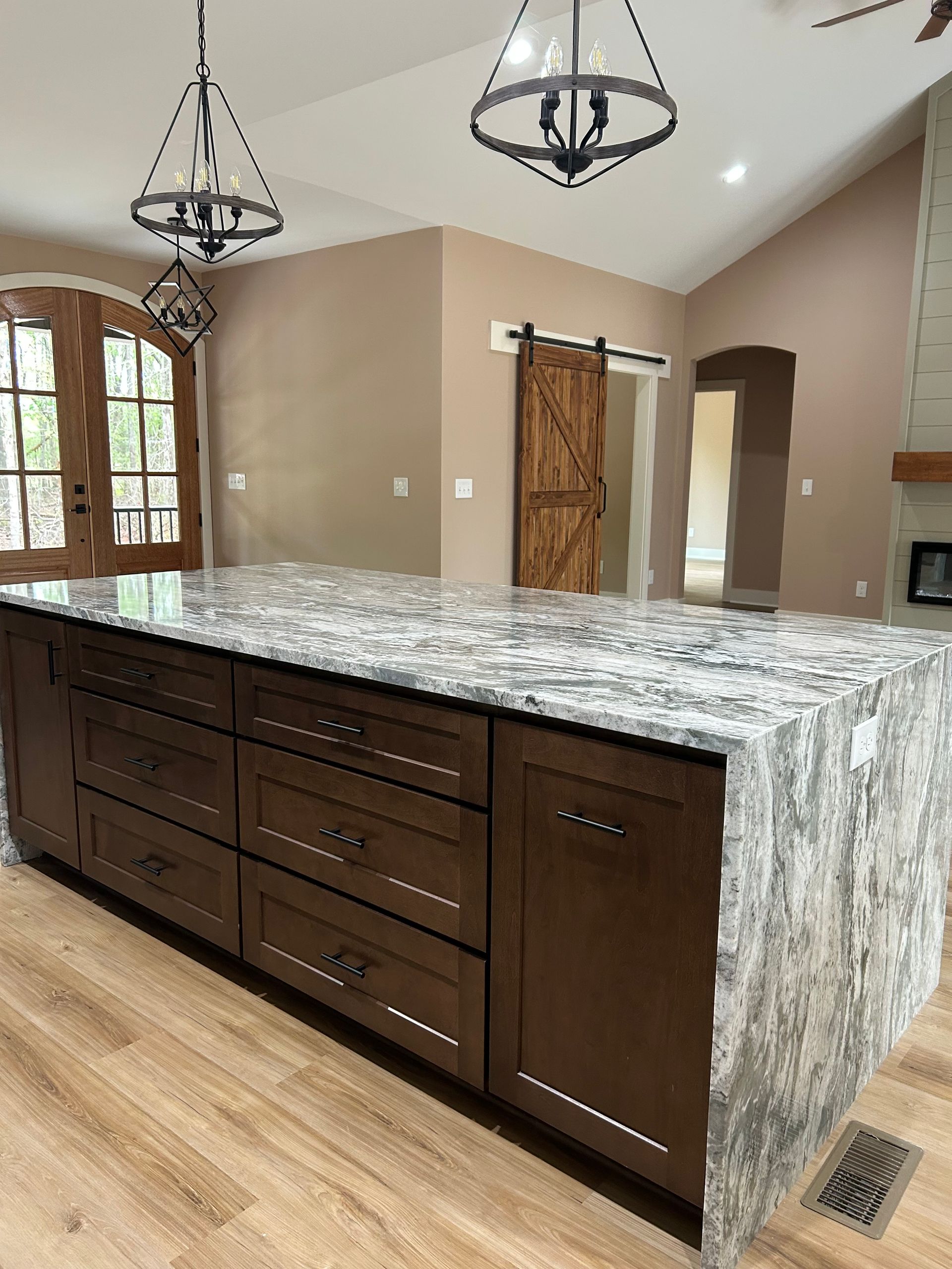 Kitchen island with dark wood cabinets, granite countertop, pendant lights, and wood flooring