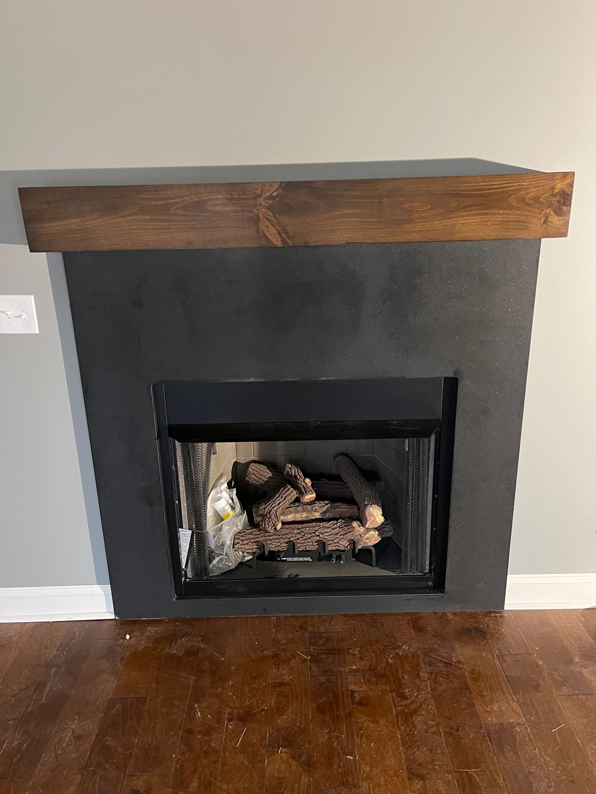 Dark gray fireplace with a thick wooden mantel and brown hardwood floor.