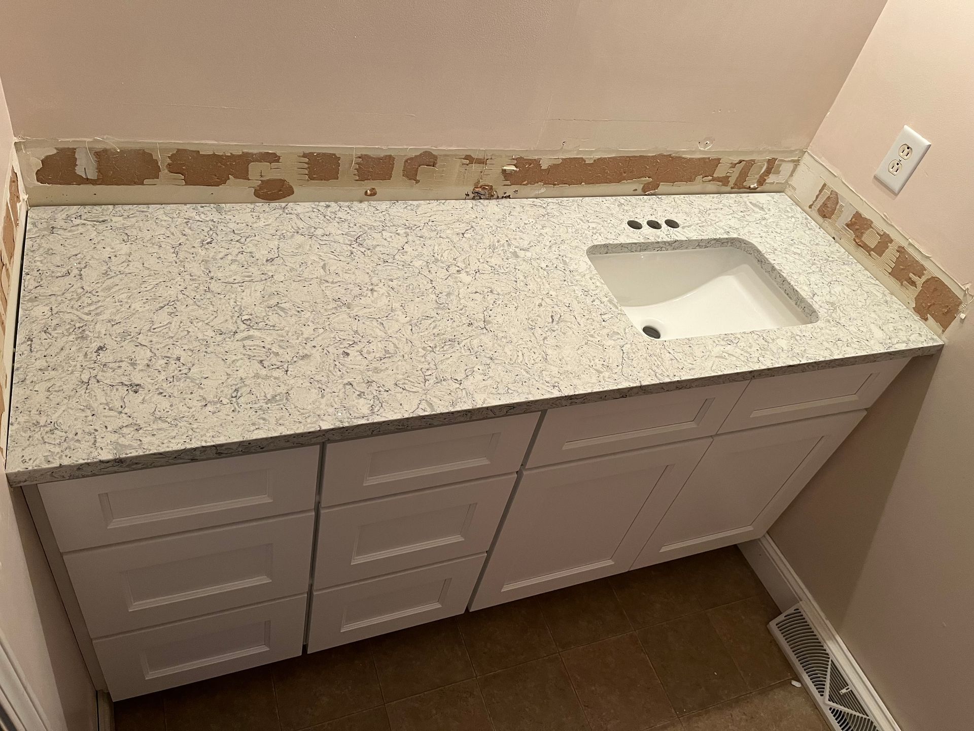 Bathroom vanity with speckled countertop, sink on the right, and white cabinets below.