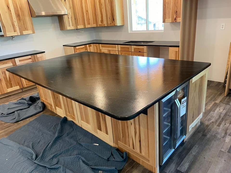 Kitchen island with dark countertop, wood cabinetry, and a built-in wine cooler under construction