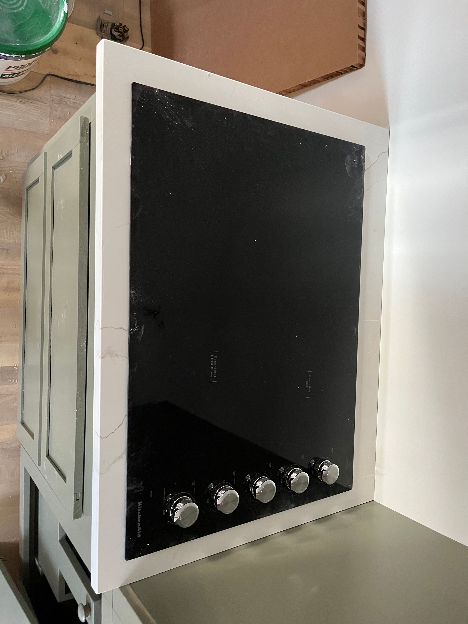 Black stovetop oven or cooker with silver knobs, standing in a kitchen beside a white wall.