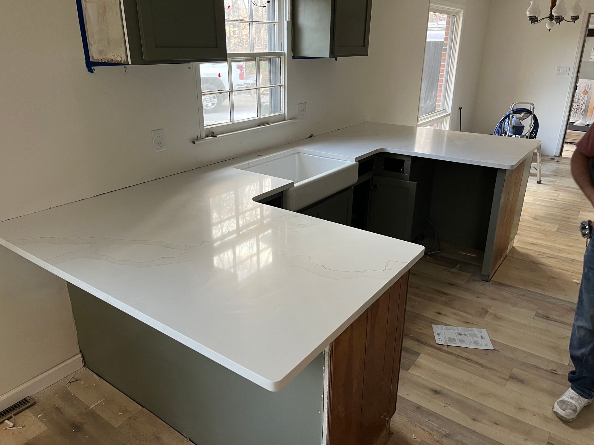 White L-shaped kitchen countertop installation with sink cutout and exposed cabinetry in a room under renovation