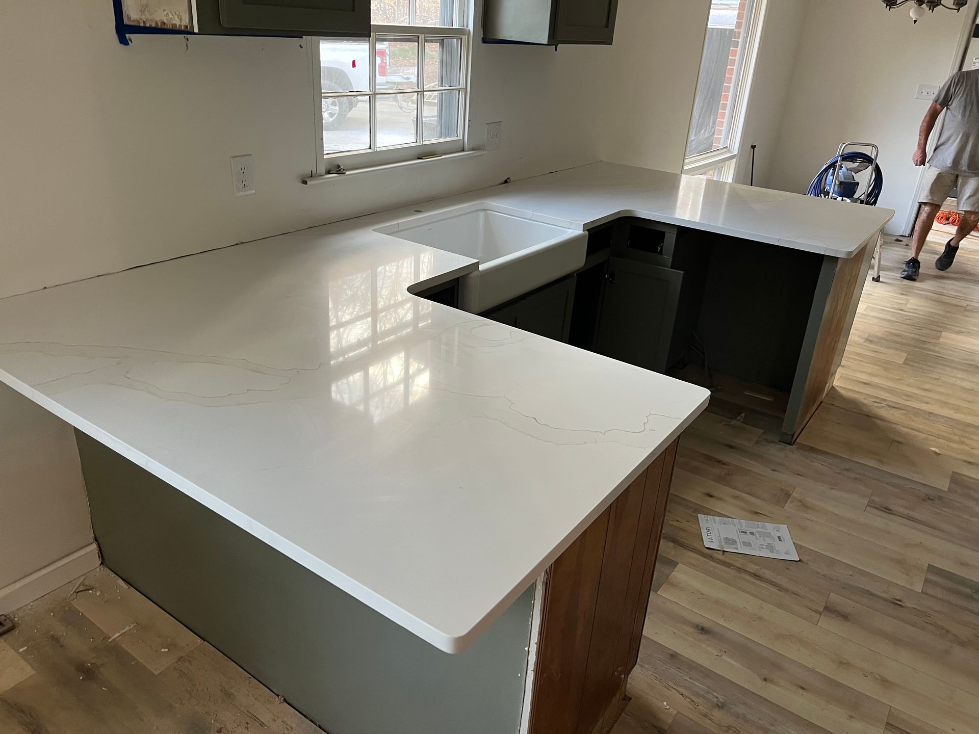 White kitchen island with glossy countertop and wood base under construction, beside a window and open floor.