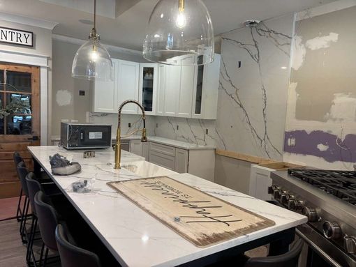 Modern kitchen with white island, pendant lights, marble backsplash, and partially renovated wall
